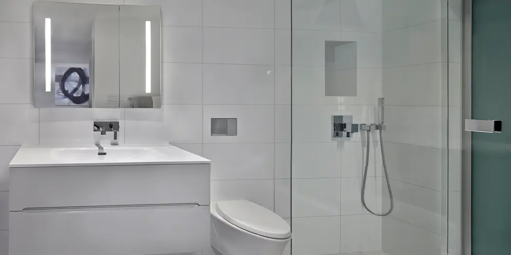 This renovated bathroom offers an immaculate, contemporary aesthetic characterized by its minimalist design and smart functionality. The space maximizes modern elegance with a focus on clean lines and a neutral color palette. A sleek floating vanity and integrated lighting system provide a sophisticated touch, while frameless glass shower doors ensure an open and airy feel. The blend of polished surfaces and understated design elements creates a spa-like retreat within the home.