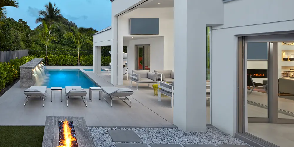 The outdoor living and pool area of this home exudes modern luxury, combining functionality with aesthetic charm. A sleek, linear design is emphasized throughout, from the clean lines of the pool to the minimalist landscaping and contemporary furnishings. This outdoor space serves as an elegant extension of the home’s interior, prioritizing both relaxation and entertainment. The integration of a fire feature and strategically placed seating enhances the ambiance, creating a seamless blend of comfort and sophistication.