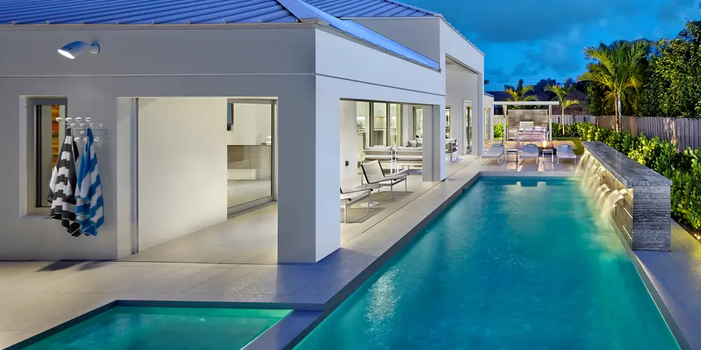 This modern poolside retreat perfectly complements the home's contemporary design, offering an oasis of relaxation and entertainment. The sleek architecture features a linear pool enhanced by an adjoining spa, seamlessly extending the indoor living space to the outdoors. The inclusion of water features, such as a cascading wall, adds auditory and visual tranquility to the environment, while ample shaded areas provide comfortable lounging and dining options.
