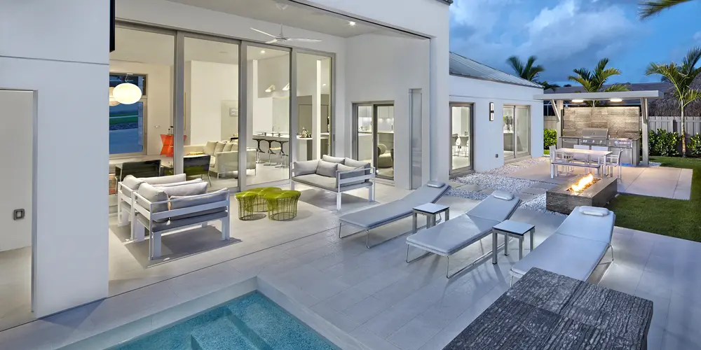 This outdoor living space exemplifies sophisticated modern design, seamlessly extending the home’s interior elegance to the outdoors. The area is defined by its open, fluid layout, featuring a luxurious spa adjoining the pool, comfortable lounging options, and a central fire feature for warmth and ambiance. Large sliding glass doors ensure seamless indoor-outdoor connectivity, enhancing the area’s functionality and appeal for both relaxing and entertaining.