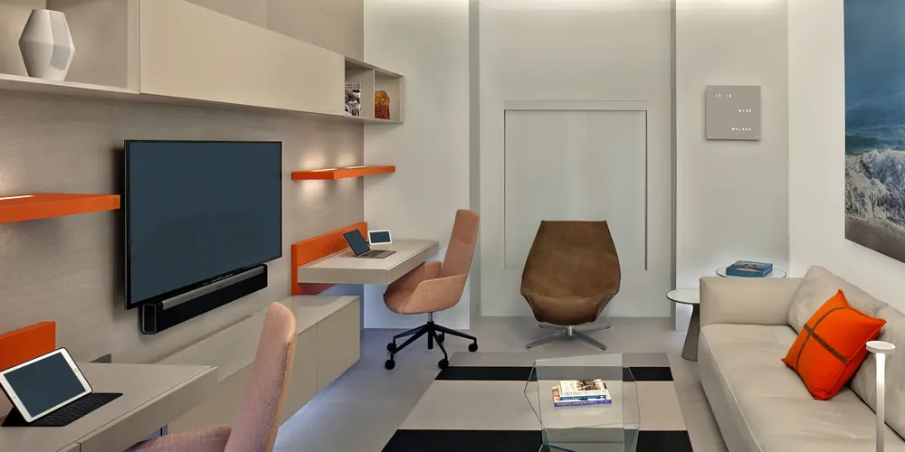 This dual home office space is meticulously designed to foster productivity and creativity, accommodating two users with individual workstations that blend functionality with modern elegance. The room features a soothing neutral palette accented with vibrant splashes of orange, which add energy and personal touch. The integration of modern furnishings and efficient organization solutions ensures that the space remains both comfortable and stimulating, ideal for focused work or collaborative projects.