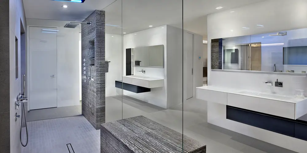 he master bathroom exemplifies luxury and modernity, featuring a spacious walk-in rain shower enclosed in seamless glass, and dual sinks that emphasize functionality and sophisticated design. The room is marked by its use of sleek, minimalist lines and a monochromatic color palette, creating a serene and spa-like atmosphere. High-end materials and strategic lighting contribute to an effortlessly chic aesthetic, offering both style and comfort for daily routines.