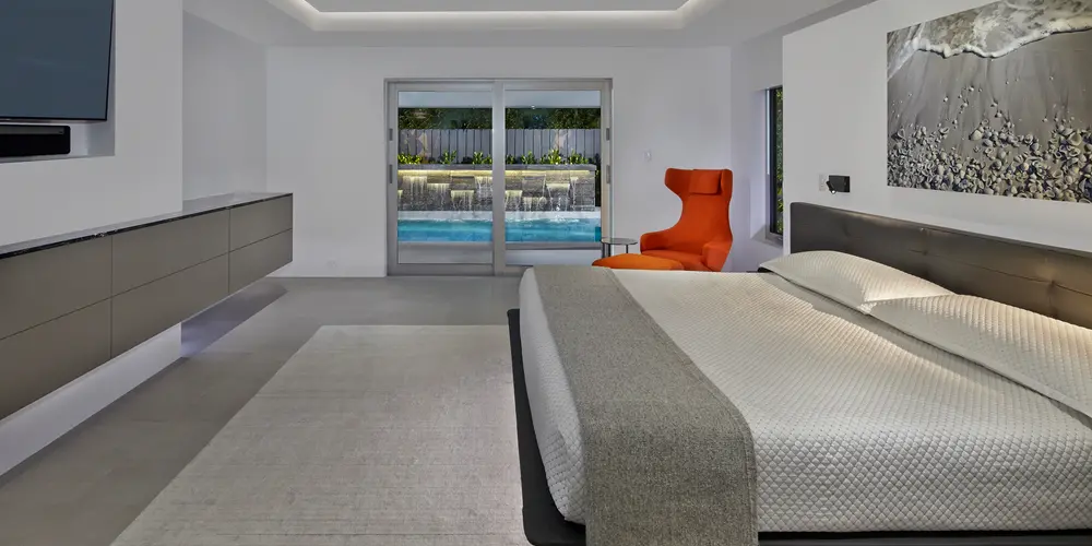 The master bedroom embodies modern elegance and offers a tranquil retreat, featuring a sleek design and thoughtful layout that maximizes comfort and luxury. Dominated by a calming neutral palette, the room is accentuated by understated yet sophisticated furnishings, creating a serene and inviting ambiance. A prominent feature is the seamless connection to the outdoor pool area, achieved through sliding glass doors that enhance the sense of openness and provide natural light.