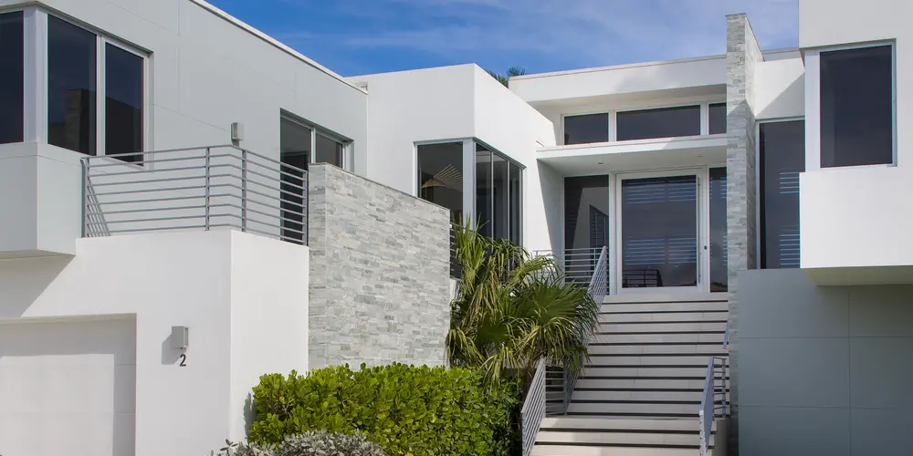 The home's entrance features a bold modern facade with clean lines and stone accents. Ascending steps and lush greenery create an inviting and sophisticated welcome to the residence.
