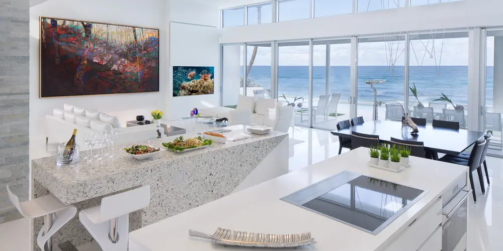 The open kitchen and dining space features expansive glass walls that frame the ocean, enhancing the room with plenty of natural light and ocean views. Sleek countertops and modern cabinetry focus on luxurious simplicity and functionality.

