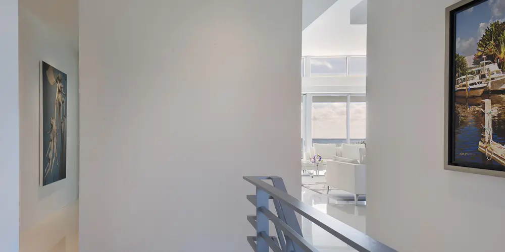 This image showcases the hallway's clean, modern lines and abundant natural light, which gracefully leads toward a living area with ocean views, balancing artful elements with architectural simplicity.
