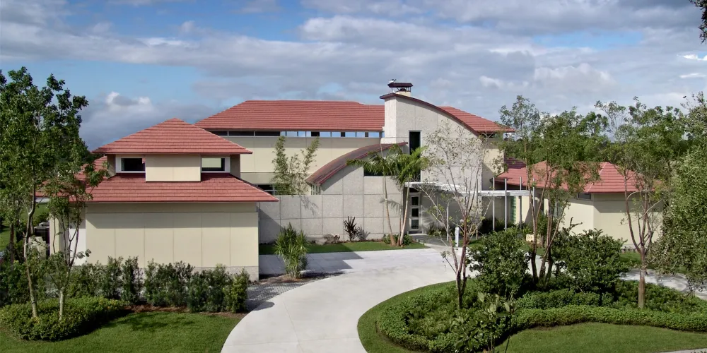 The architecture of Hills House features a combination of angular and curved geometric forms. The red roofing against soft-toned walls creates a harmonious palette with the surrounding greenery.