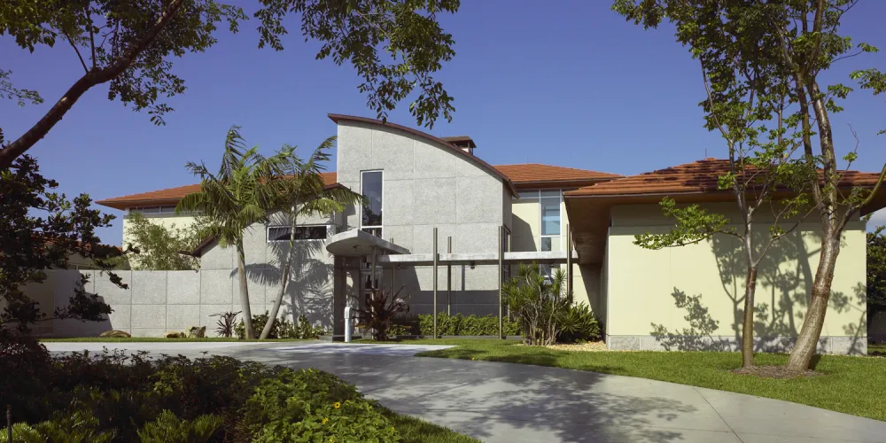 The entrance of Hills House is defined by sleek, modern lines and a welcoming pathway lined with lush greenery. A balanced blend of solid surfaces and transparent elements characterizes the entryway, emphasizing the use of natural materials and careful landscaping.
