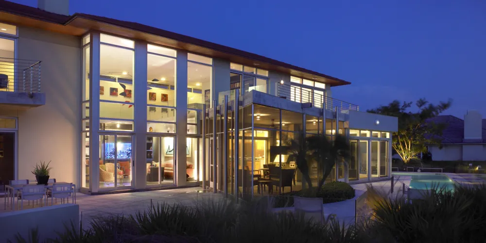 Illuminating against the night sky, the Hills House presents a striking façade of glass walls revealing the warm interior aesthetics. The combination of artificial lighting with natural elements creates an elegant and contemporary look, perfectly suited for evening relaxation and gatherings.
