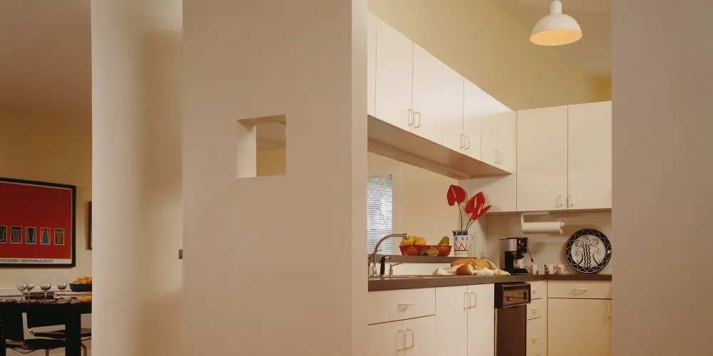 A quaint, alcove kitchen combines functionality with charm, featuring warm wood flooring and clean lines. White cabinetry exudes simplicity, while pendant lights offer gentle illumination. This compact space is inviting, filled with warmth and practicality, encouraging culinary creativity without compromising style.