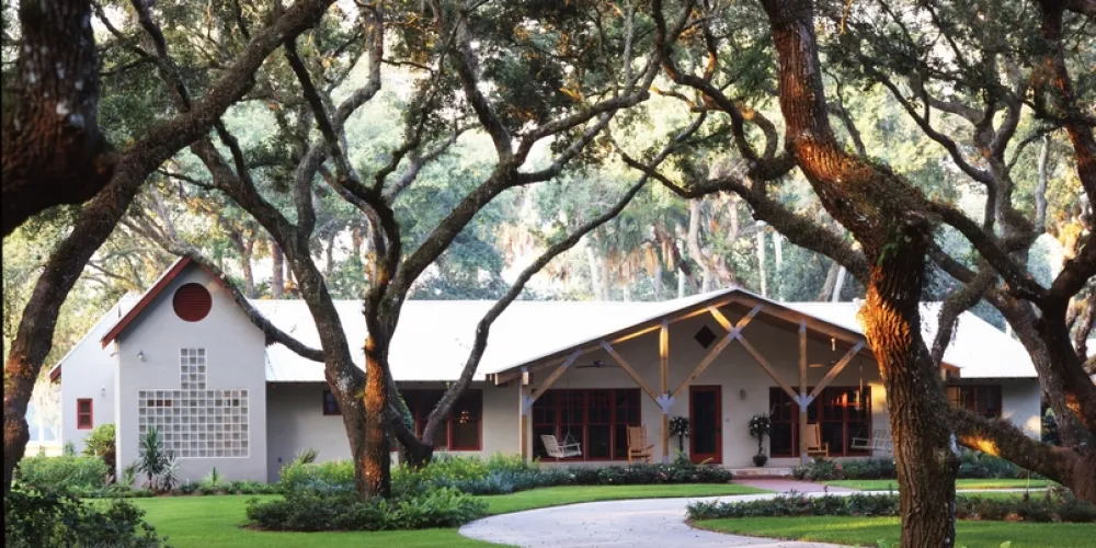 From a distance, the driveway view underscores the holistic design approach, with the renovated home seamlessly fitting into its lush environment. The clear lines and extensive use of wood exemplify a contemporary take on the classic ranch house, presenting a refined curb appeal.