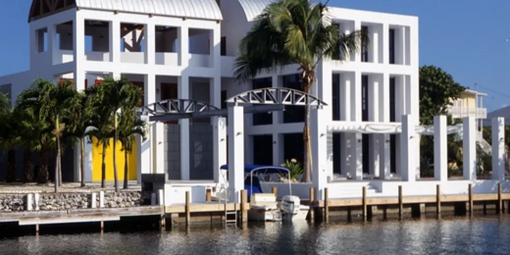 A striking modern residence with clean white lines and extensive glasswork, nestled by the tranquil waters, exemplifies a contemporary architectural aesthetic, ideal for luxurious waterfront living.
