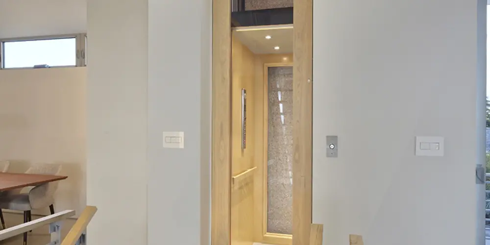 This home boasts an integrated modern elevator within a clean, minimalist space. The interplay of wood and neutral colors creates a warm contrast within the predominantly white interiors, allowing natural light to infuse the area, enhancing the sense of vertical space and modernity.
