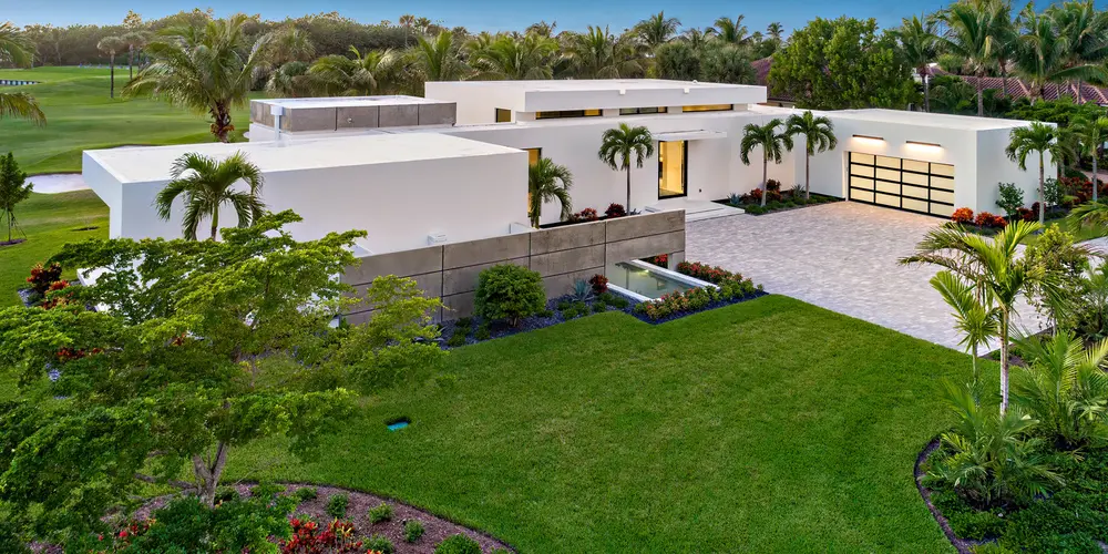 The house’s layout is revealed in all its geometric elegance, offering a perfect interplay between architecture and the meticulously landscaped garden. The color contrast between the building and verdant surroundings is striking and visually appealing.
