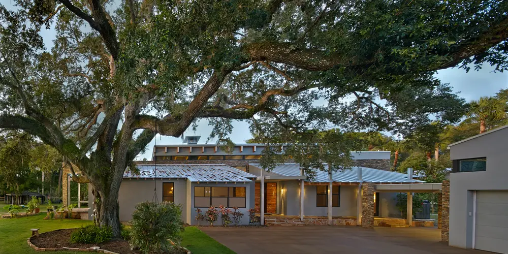 Nestled beneath the embracing boughs of a venerable tree, this distinctive architectural marvel exemplifies the serene synthesis of environmental consciousness and modern aesthetics. The residence's facade, bathed in the gentle hues of earth-toned plaster, harmonizes subtly with the surrounding landscape, offering an inviting sensory experience.