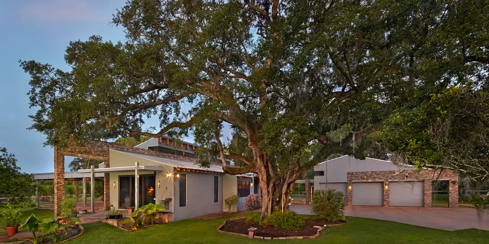 A serene residential scene where architecture and nature coalesce beautifully under the canopy of a majestic tree. The home is strategically nestled within its verdant surroundings, emphasizing an organic integration with the natural environment.