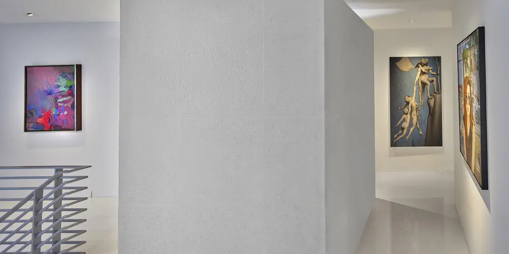 This interior gallery corridor is marked by a minimalist design, featuring clean, white walls that function as a backdrop for vibrant art pieces. The strategic display of artwork adds a dynamic cultural flair, creating an inviting path that leads further into the home.
